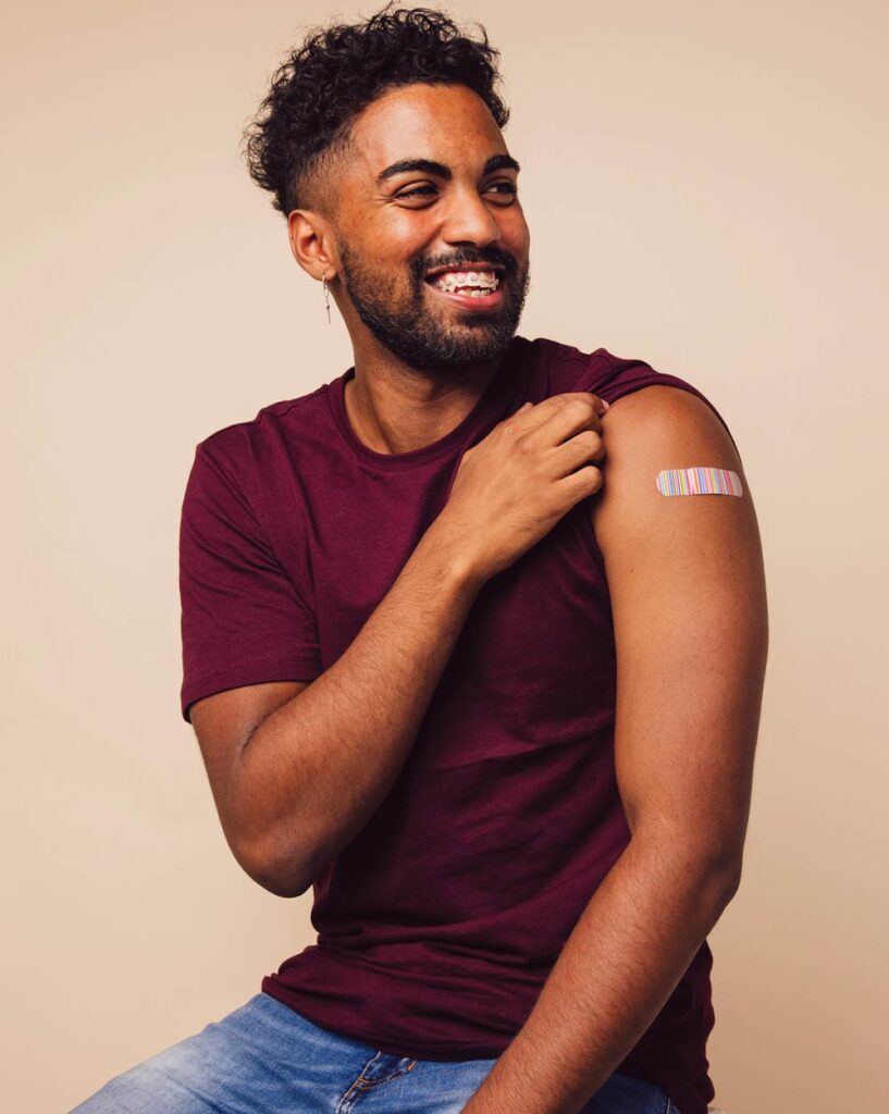Happy young man smiling while lifting his sleeve to show a bandaid on his arm