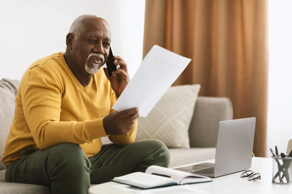Senior Black Businessman Talking On Phone Holding Papers Working Indoors